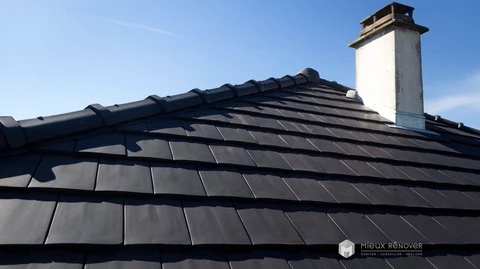 Toiture en pente raide recouverte de tuiles plates en béton coloris anthracite/ardoise, disposées en rangées régulières avec recouvrement