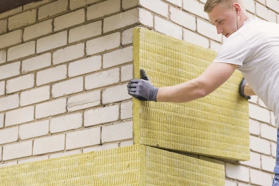 Chantier de construction extérieur avec ouvriers en gilets haute visibilité jaune et orange installant l'isolation et la couverture d'une toiture en pente